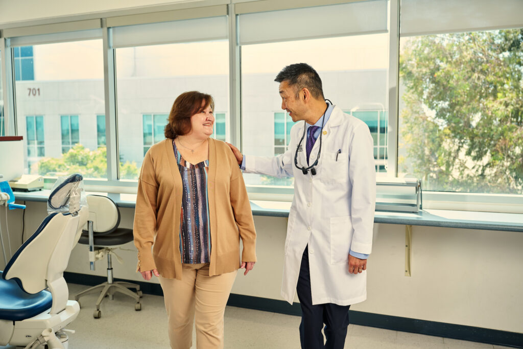 A female patient walking beside a male dentist in a treatment room inside the dental center